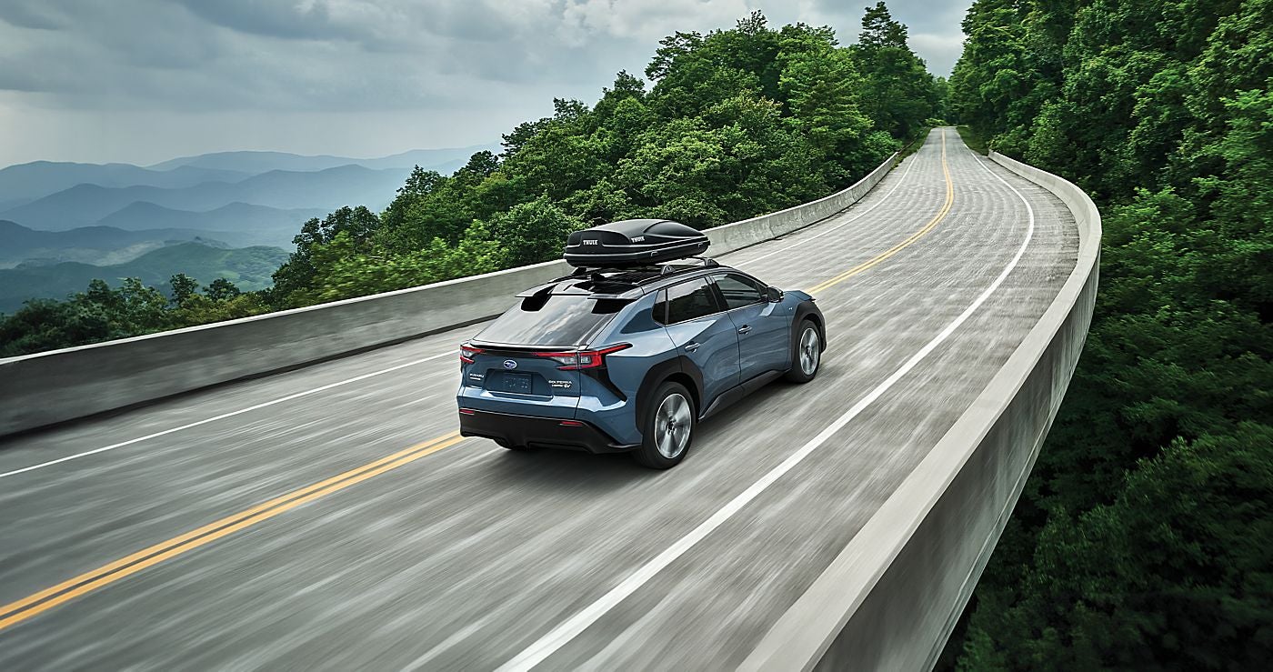 A SUV driving across a bridge surrounded by lush green trees.