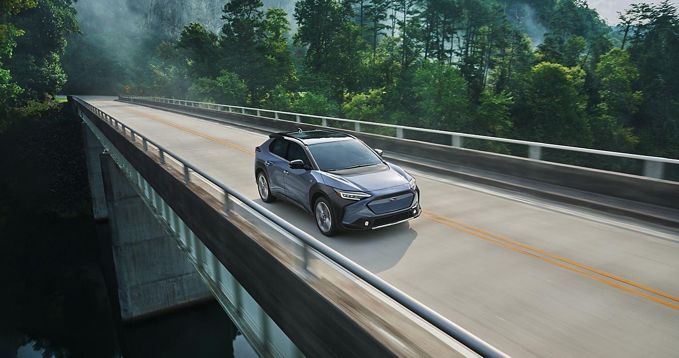 A SUV driving across a bridge surrounded by lush green trees.
