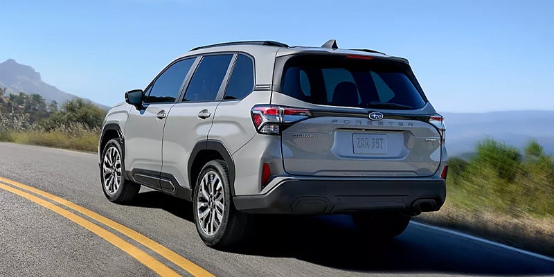 Rear view of a light-colored SUV driving down a sunny, paved road