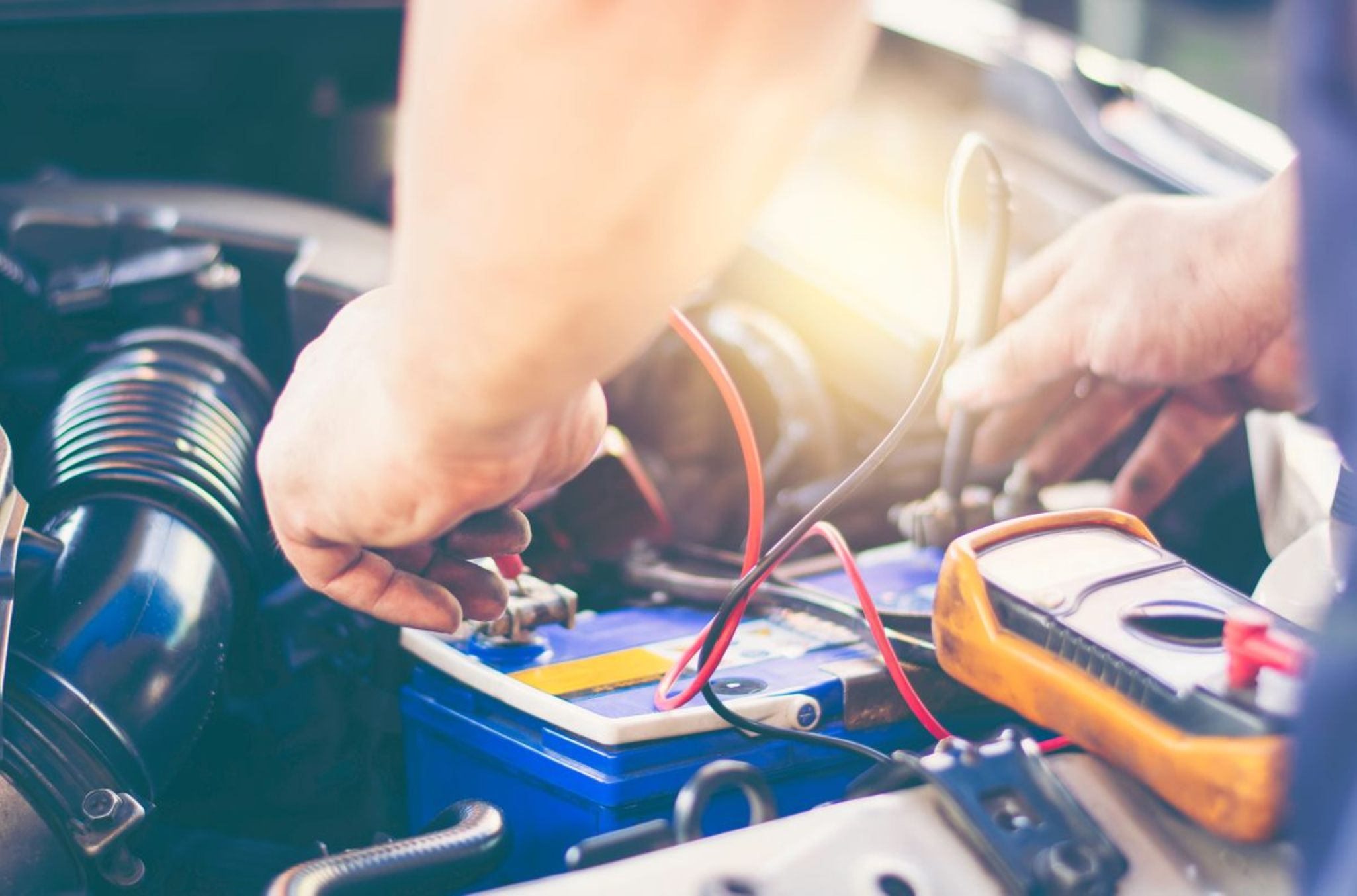 A person works on a car battery under the hood, connecting electrical cables near the battery.