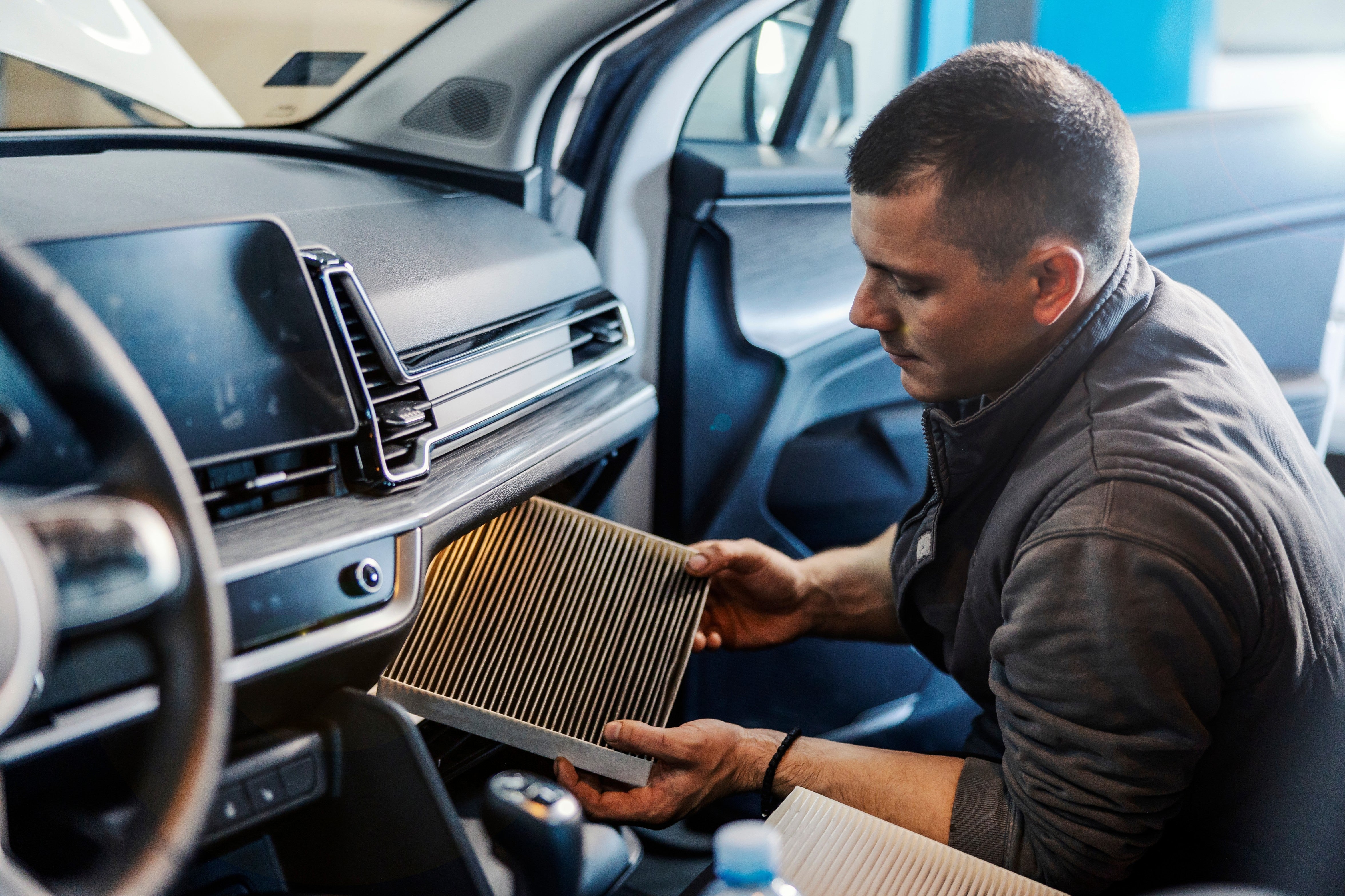 Automotive technician replacing a cabin air filter inside a vehicle during a maintenance service.